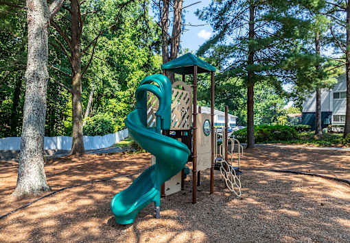 A green slide in a playground surrounded by trees.