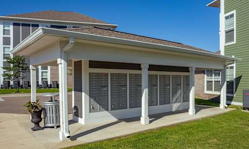 A small white building with a porch and a trash can in front of it.