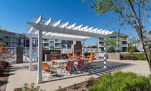 A white pergola with orange chairs is in front of a building.