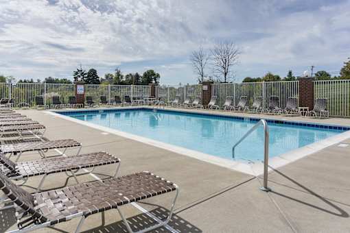 A pool surrounded by sun loungers and a metal fence.