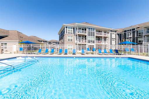 Alexandria, KY, Apartments Near National Harbor - Elevation Apartment Homes - Swimming Pool With Bright Blue Water, Blue Lounge Chairs, White Fencing, and Umbrella Seating.