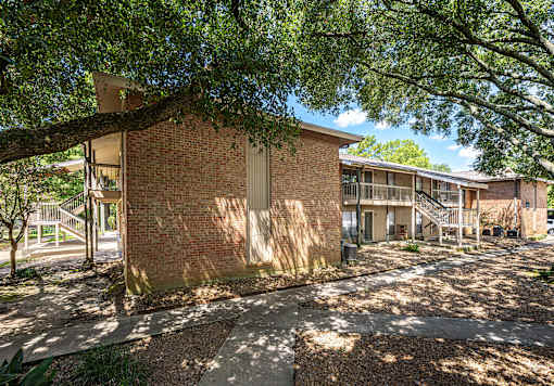 A tree shades a walkway in front of a brick building.