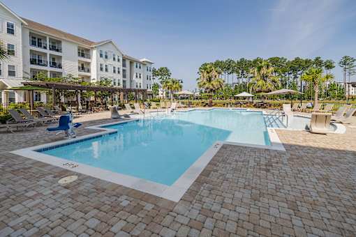 A large swimming pool surrounded by a brick patio and lounge chairs.