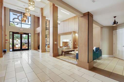 A large, open living room with a white tile floor and a glass door leading to a balcony.