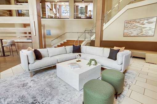 A white sofa with a green ottoman and a white coffee table in a spacious room.