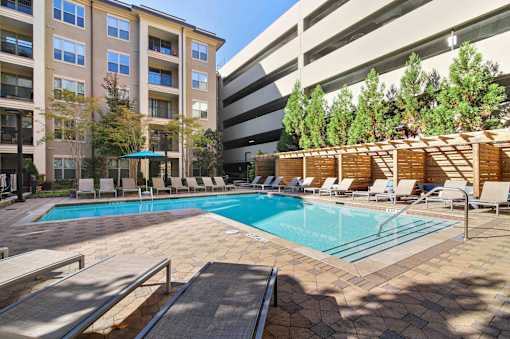 Atlanta, GA, Luxury Apartments with In-Unit Washer and Dryer - 1105 Town Brookhaven - Resort-Style Swimming Pool with Sundeck, Lounge Seats, Cabanas, Trees, and View of Apartment Building.