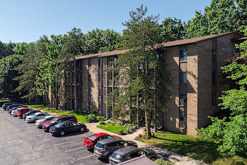 A parking lot with cars parked in front of a building with trees in the background at Winchell Way Apartment , Kalamazoo, 49008