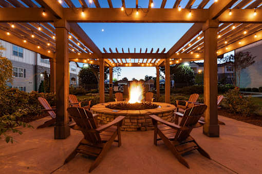 A patio with a fire pit and chairs under a pergola.