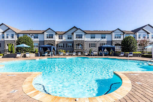 Two-Bedroom Luxury Apartments In Greenville, SC - The Aventine Greenville - A Large, Clear Blue Community Pool With Poolside Cabanas And Lounge Chairs In Front Of Stone-Accented Apartment Buildings.