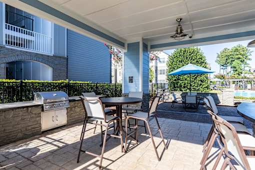 Luxury Apartments In Greenville, SC With In-Unit Washer And Dryer - The Aventine Greenville - A Covered Outdoor Grilling Station With A Stainless Steel Grill, Stone Masonry, And Patio Dining Tables.