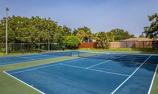 A tennis court surrounded by trees and a fence.