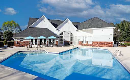 Charlotte, NC, Apartments Near ALDI - Coffey Creek - A Bright Outdoor Swimming Pool With Brick Accents, Patio Seating, Blue Umbrellas.