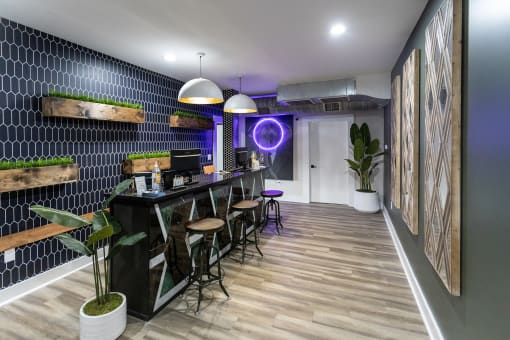 a room with a bar and stools in front of a black tiled wall with a