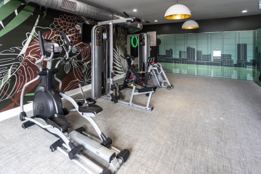 a gym with cardio equipment and a mural of a city on the wall