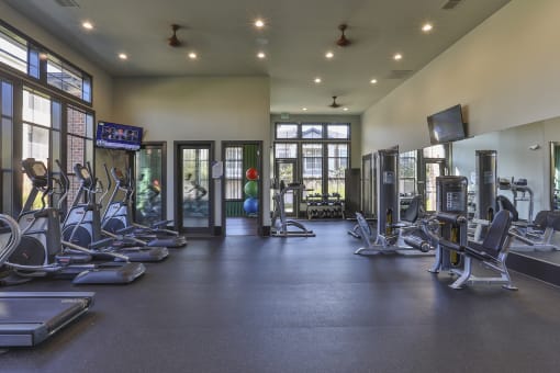 the fitness center has cardio equipment and weights in a large room with windows