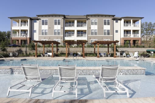 a large swimming pool with rocking chairs in front of an apartment building
