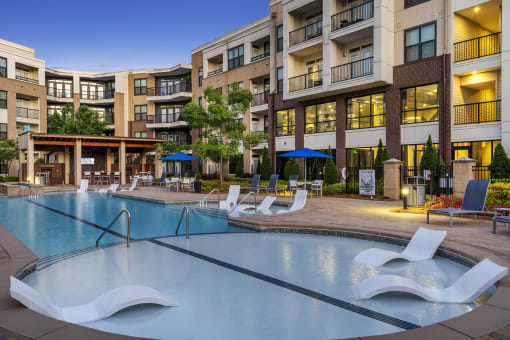 a swimming pool with lounge chairs in front of an apartment building