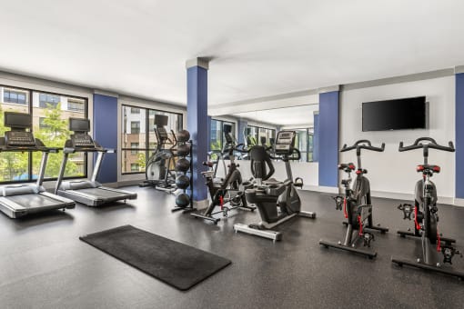 a gym with treadmills and other exercise equipment in a room with windows