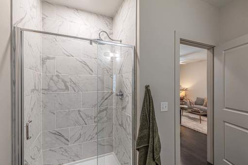 A bathroom with a marble tile shower and a green towel hanging on the door.