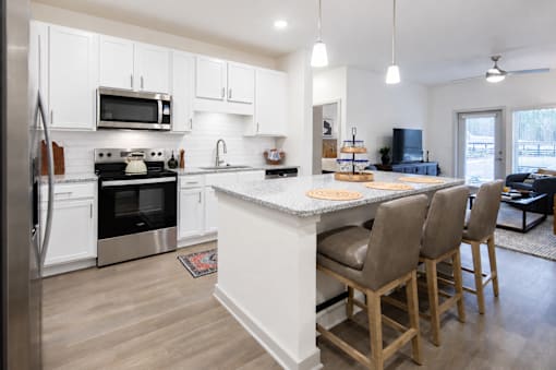 A modern kitchen with a white island and wooden chairs.