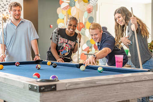 Four people playing pool in a room with balloons.