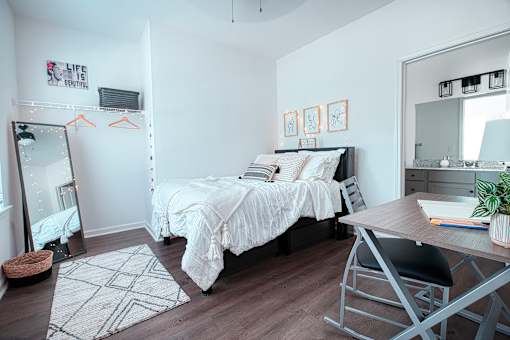 A bedroom with a white bed and a wooden desk.