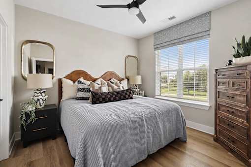 A bedroom with a bed, dresser, mirror, and window.