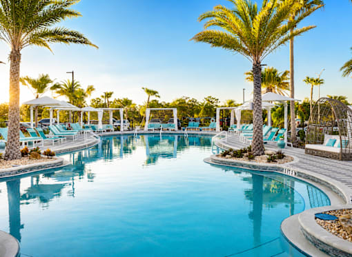 A large outdoor swimming pool surrounded by palm trees and lounge chairs.