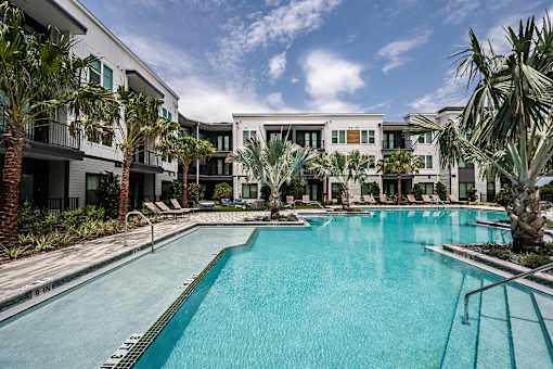 A swimming pool in front of a building with palm trees.