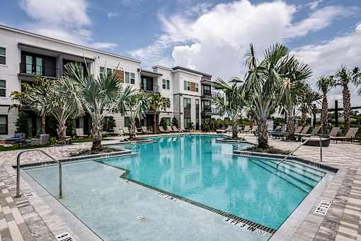 A swimming pool surrounded by palm trees and lounge chairs in front of a modern building.