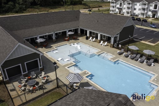 an aerial view of a swimming pool and a building with tables and umbrellas