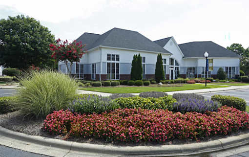 A white building with a grey roof is surrounded by a flower bed.