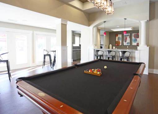 A pool table in a room with a bar and chairs.