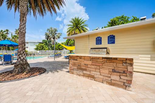A yellow building with a stone wall and a palm tree in front at Coral Club Apartments in Bradenton, FL