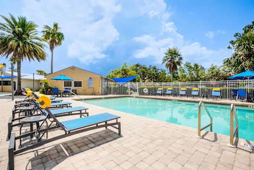 A pool area with sun loungers and a yellow building in the background at Coral Club Apartments in Bradenton, FL