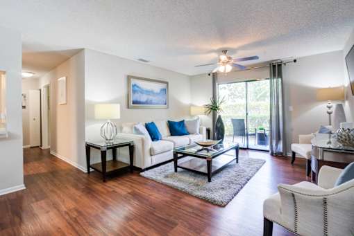 A living room with a white couch and a painting on the wall at Coral Club Apartments in Bradenton, FL