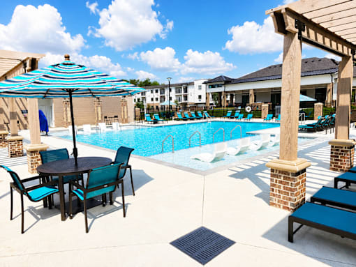 A pool area with a table and chairs and umbrellas.