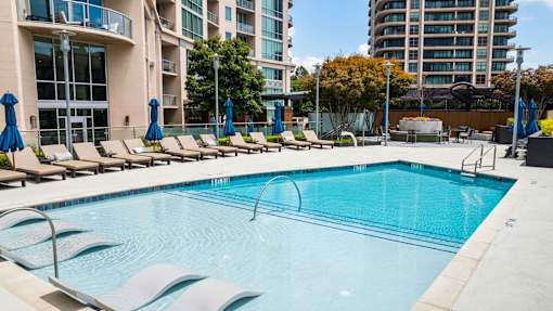 A swimming pool surrounded by lounge chairs and umbrellas in a sunny outdoor setting.