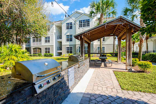 a patio with a grill and a picnic area with a building in the background