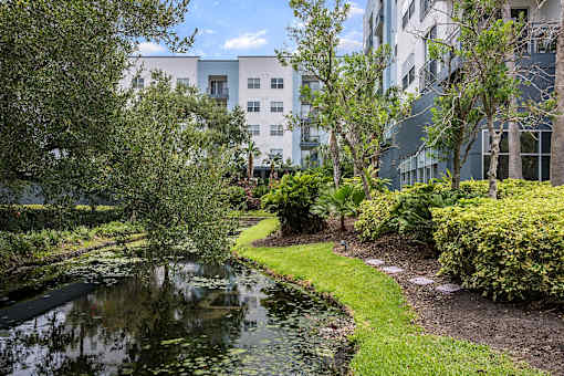 A pond in the middle of a grassy area with a building in the background.