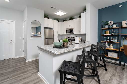 Apartments in Alexandria, KY, with In-Unit Washer and Dryer - Elevation Apartment Homes - Kitchen With Granite Island Seating, White Cabinets, Stainless Steel Appliances, And Accent Shelving.