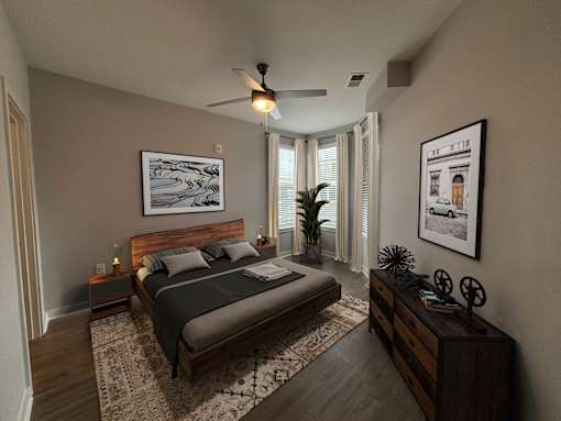 Two-Bedroom Apartments in Mt. Juliet, TN - The Enclave at Providence - Bedroom with Hardwood-Style Flooring, Large Bed, Dresser, Nightstands, Lamps, Wall Paintings, Ceiling Fan, and Large Windows.