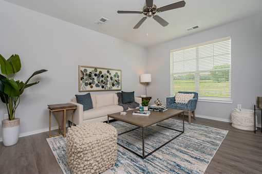 A living room with a white ceiling fan and a large window with blinds.