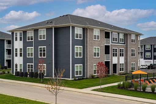 Apartment building with grey and white exterior and a small tree in front.