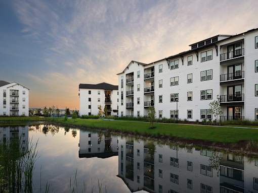 A modern apartment complex is reflected in a calm body of water.