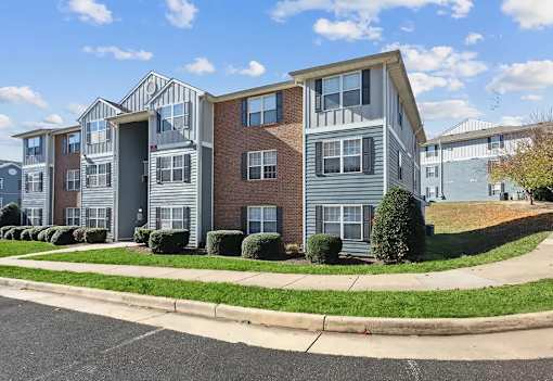 A row of townhouses with a sidewalk and green bushes in front.