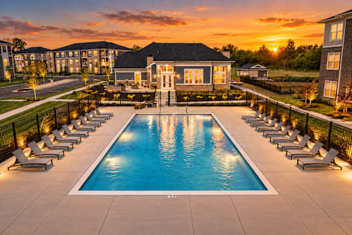 A large swimming pool surrounded by lounge chairs and a building in the background.