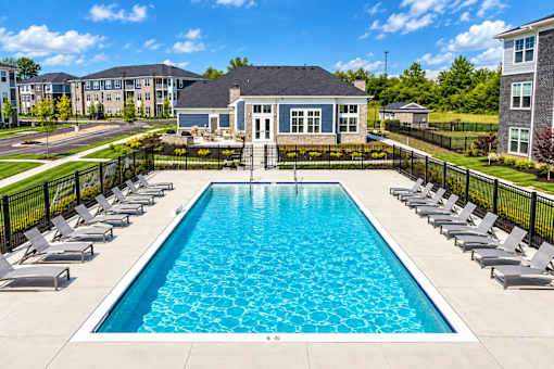 A large swimming pool surrounded by lounge chairs and a building in the background.