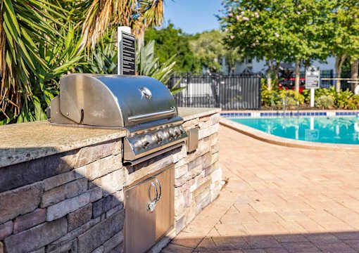 A silver barbecue grill is on a stone wall next to a pool.