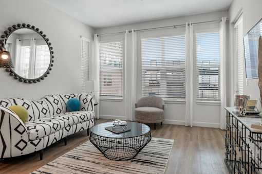Luxury Apartments Near St. Pete Oak & Stone - Gallery 3100 - A Bright, Modern Living Room Featuring A Geometric-Patterned Sofa, A Round Wire Coffee Table, And Large Windows With White Sheer Curtains.